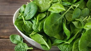 Folhas frescas de espinafre em uma tigela branca sobre superfície de madeira, destacando a cor verde intensa e o aspecto natural do alimento.