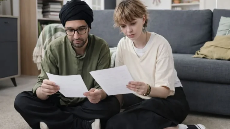 Casal Sentado No Chão De Casa Analisa Contas E Documentos Financeiros No Início Do Ano, Em Ambiente Doméstico.