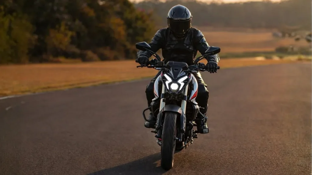 Bajaj Dominar Ns400Z Em Ação, Vista Frontal, Com Piloto Equipado Em Estrada Aberta, Destacando O Visual Agressivo Da Naked Esportiva E Iluminação Full Led.