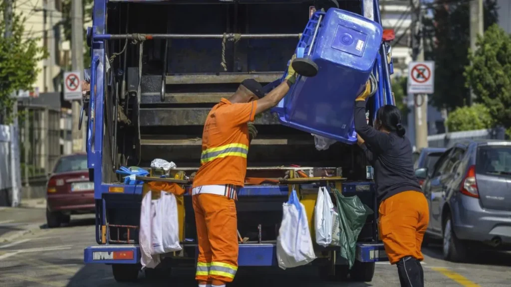 Trabalhadores Realizam A Coleta De Resíduos Urbanos Com Caminhão Compactador Em Via Pública, Ilustrando A Etapa Mais Visível Do Sistema De Gestão Do Lixo Nas Cidades.