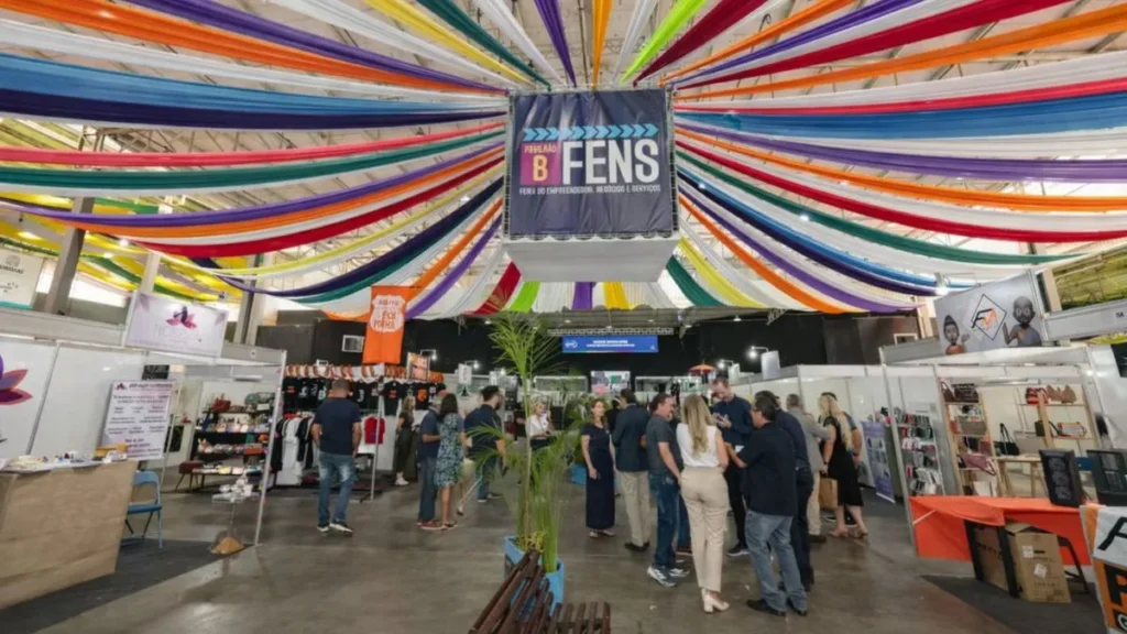 Visitantes Circulam Entre Estandes Da Feira Fens No Parque Da Uva, Em Jundiaí, Com Decoração Colorida Suspensa No Teto E Ambiente Movimentado