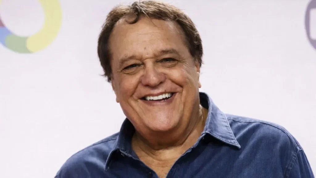 Denis Carvalho Sorrindo Em Evento Público, Usando Camisa Azul Jeans, Em Foto Horizontal 13:9 Com Fundo Claro Desfocado