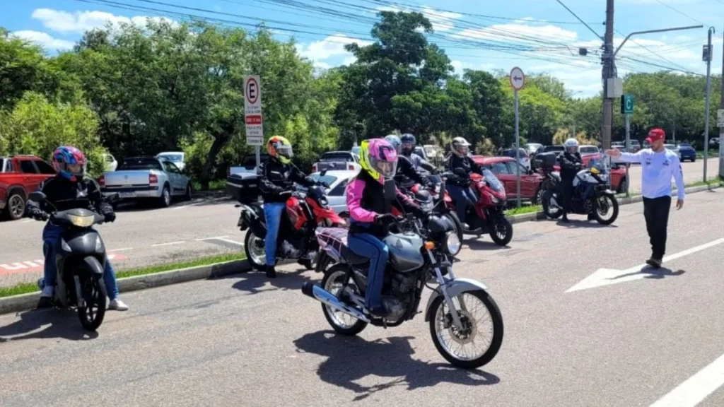 Motociclistas Participam De Treinamento De Segurança Viária Em Área Aberta Enquanto Instrutor Orienta Posicionamento E Manobras Durante Atividade Educativa.