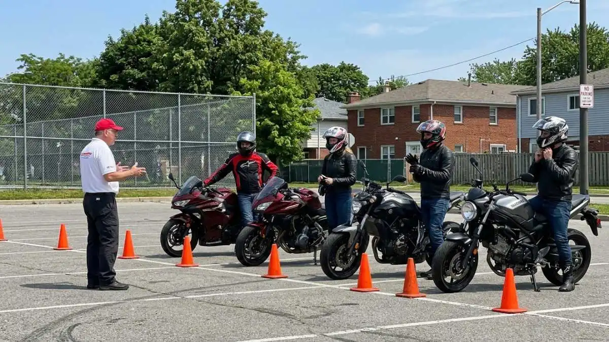 Quatro motociclistas em suas motos ouvem atentamente um instrutor em um pátio com cones, durante o Programa de Segurança do Motociclista de Jundiaí.