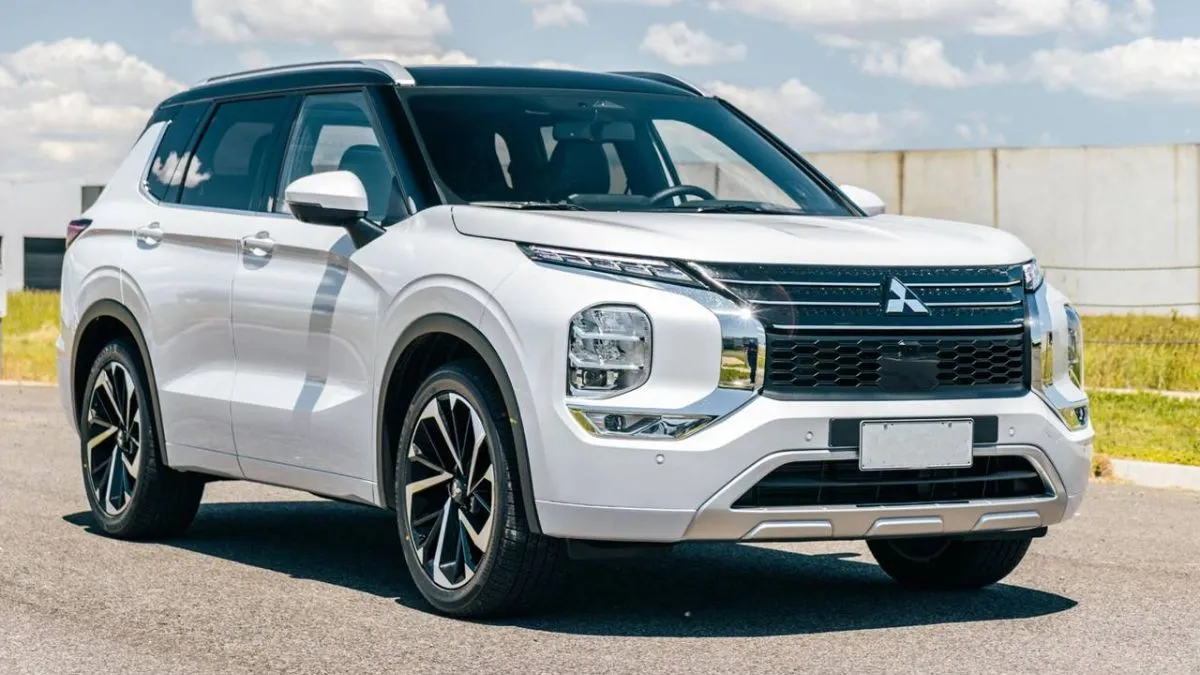 SUV Mitsubishi Outlander PHEV 2026 branco estacionado em área aberta, com design moderno, faróis em LED e rodas esportivas, sob céu azul com nuvens.