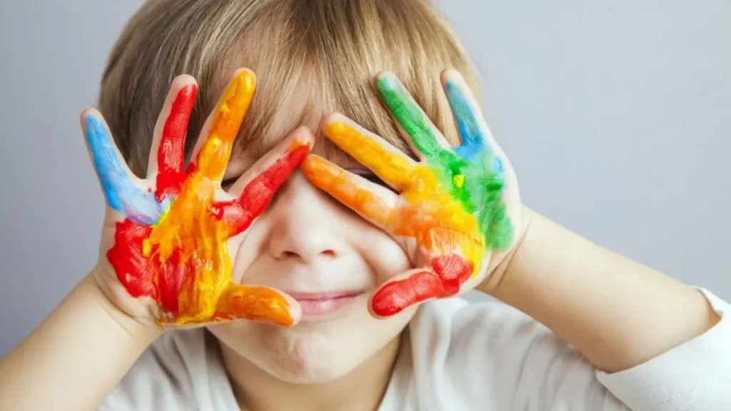 Criança Com As Mãos Cobertas De Tinta Colorida Segurando O Rosto, Simbolizando Criatividade, Inclusão E Conscientização Sobre O Autismo
