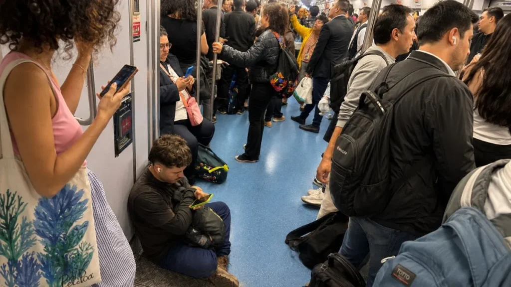 Celular Na Mão, Risco Na Rua E No Trem: A Distração Que Virou Ameaça Diária 2 Interior De Um Trem Lotado Entre As Estações De Caieiras E Barra Funda, Sp, Com Passageiros Em Pé E Sentados, Vários Olhando Para O Celular. Em Primeiro Plano, Um Homem Agachado No Chão Usa Fones De Ouvido E Segura O Aparelho, Enquanto À Esquerda Uma Mulher De Blusa Rosa Também Olha Para O Celular.