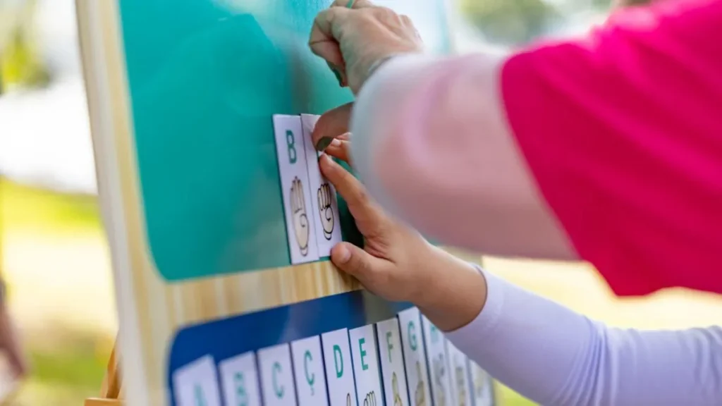 Jundiaí Prepara Centro Para Crianças Neurodivergentes Com Até Mil Atendimentos Por Mês 1 Mãos De Criança E Adulto Posicionam Cartões Com Letras E Sinais Em Um Quadro Durante Atividade Educativa Ao Ar Livre.