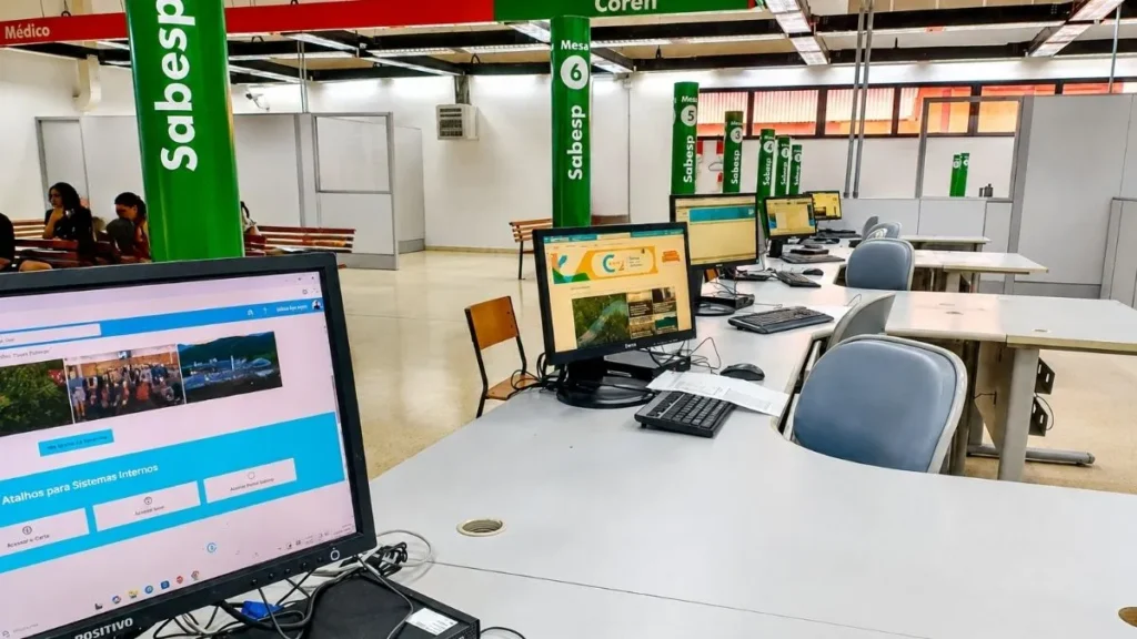 Área De Atendimento Da Sabesp Em Unidade Do Poupatempo, Com Mesas, Computadores E Sinalização Verde Da Companhia Em Espaço De Serviços Públicos.