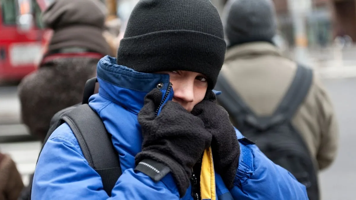 Pessoa na rua usando jaqueta de frio azul, luvas e gorro preto para se proteger da queda brusca de temperatura e vento gelado.