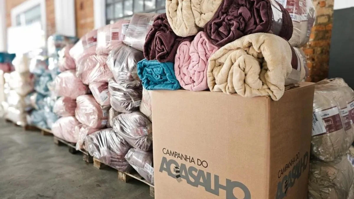 Cobertores arrecadados para a Campanha do Agasalho em caixa de coleta e pacotes organizados para distribuição.