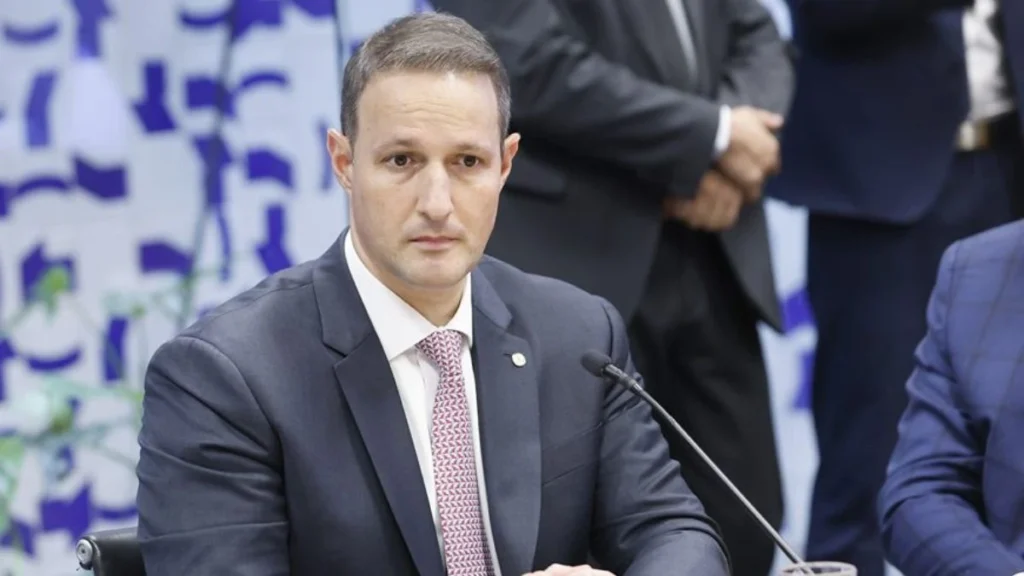 Guilherme Derrite Durante Reunião, Sentado À Mesa Com Microfone, Em São Paulo.