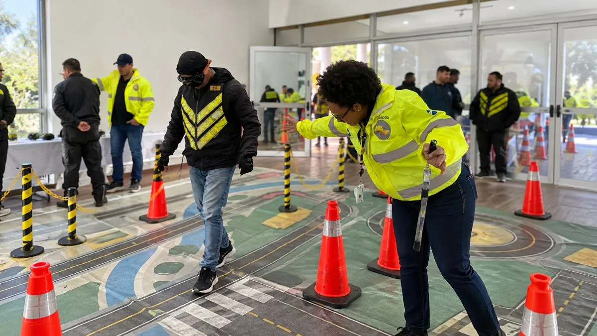 Participante usa óculos simuladores em circuito educativo enquanto equipe do DER-SP acompanha atividade de segurança viária em ambiente interno