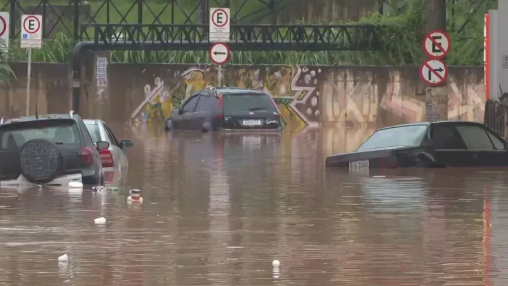 Alerta laranja atinge Caieiras e região: como se preparar para chuva forte e rajadas intensas 1 Rua urbana tomada pela água durante chuva intensa, com enxurrada avançando pela via.