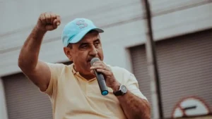 Gerson Romero de boné azul segura um microfone e ergue o punho durante discurso em ato público