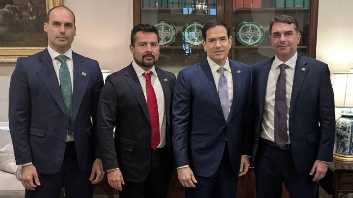 Marco Rubio, Eduardo Bolsonaro, Flávio Bolsonaro e Paulo Figueiredo posam para fotografia durante encontro em uma sala com estantes de livros e objetos decorativos ao fundo.