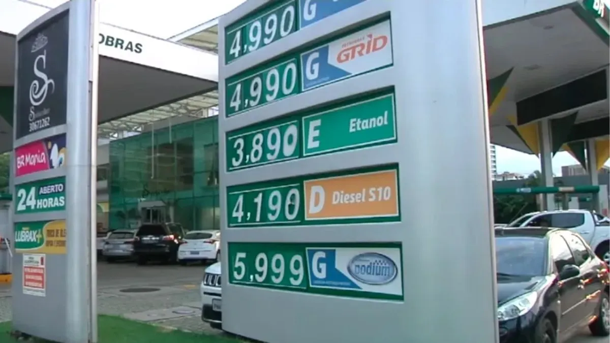 Painel de preços em posto Petrobras mostra valores de gasolina comum, etanol, diesel S-10 e gasolina Podium, com veículos ao fundo.