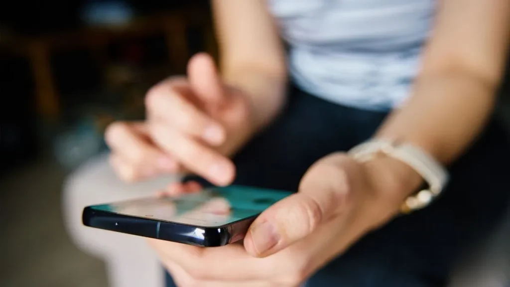 Pessoa utiliza smartphone enquanto acessa a tela do aparelho, em imagem que ilustra a atualização cadastral de linhas de celular e as novas exigências de biometria da Anatel.