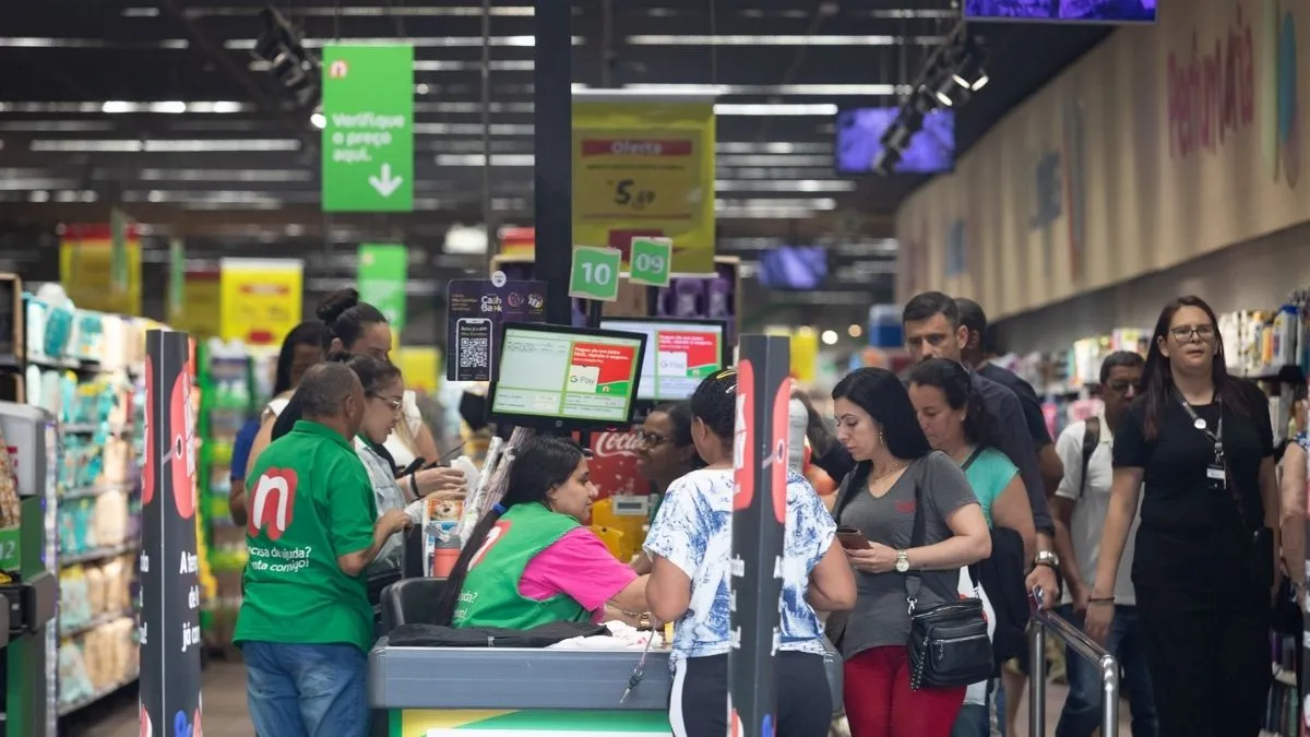 Funcionários atendem clientes nos caixas de um supermercado movimentado, ilustrando os desafios do comércio para reorganizar as jornadas com o fim da escala 6x1.