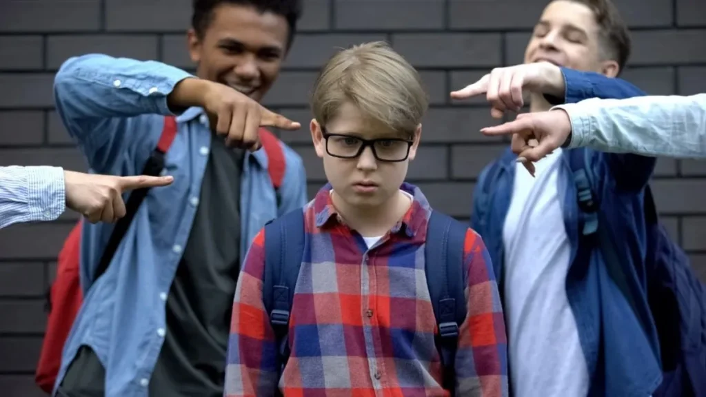 O que é bullying? Conheça os 8 tipos e quando uma brincadeira vira agressão 3 Menino de óculos e mochila aparece constrangido enquanto colegas apontam para ele e riem, em cena ilustrativa de bullying escolar.