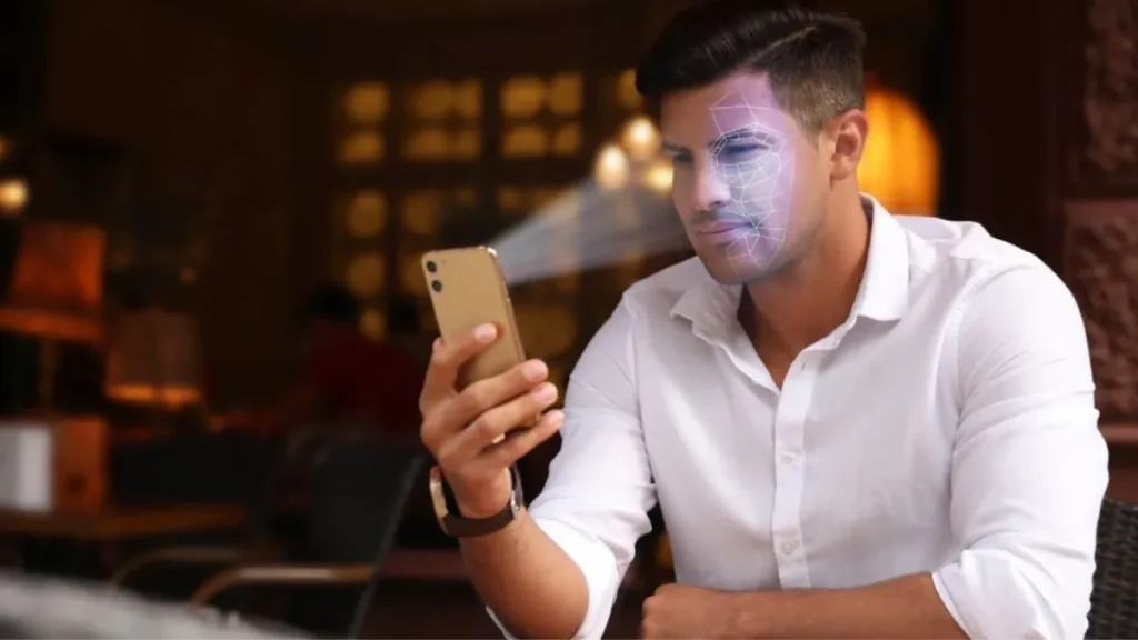 Homem de camisa branca utiliza celular para reconhecimento facial, procedimento previsto nas novas regras de validação biométrica da Anatel.